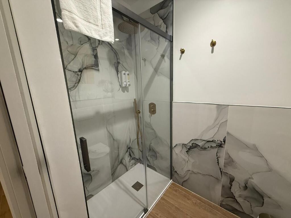 A bathroom with a glass shower enclosure, marble walls, and a towel hanging on the door.