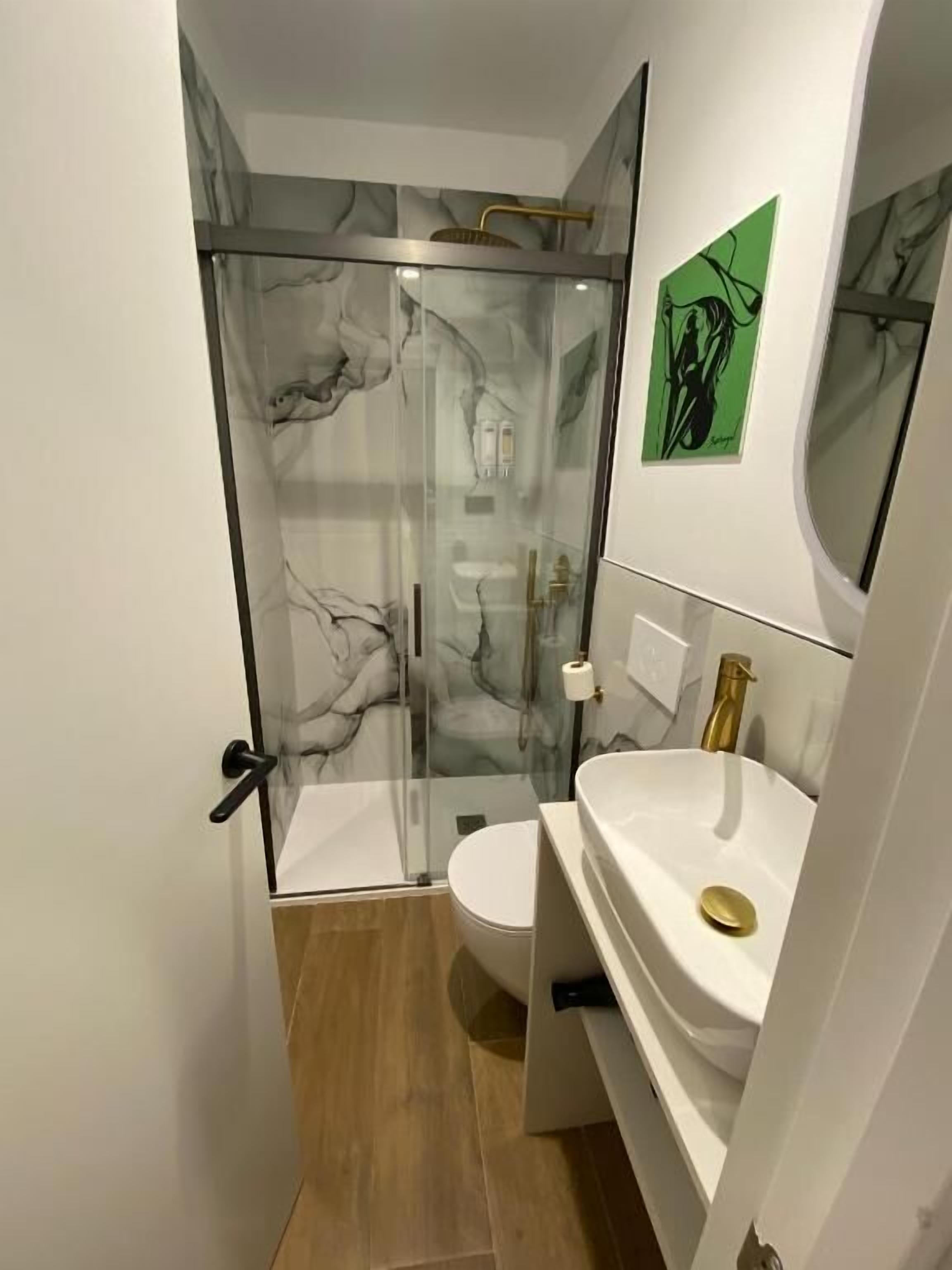 Een moderne badkamer met een douchecabine van glas, een wit toilet en een witte wastafel met gouden details.