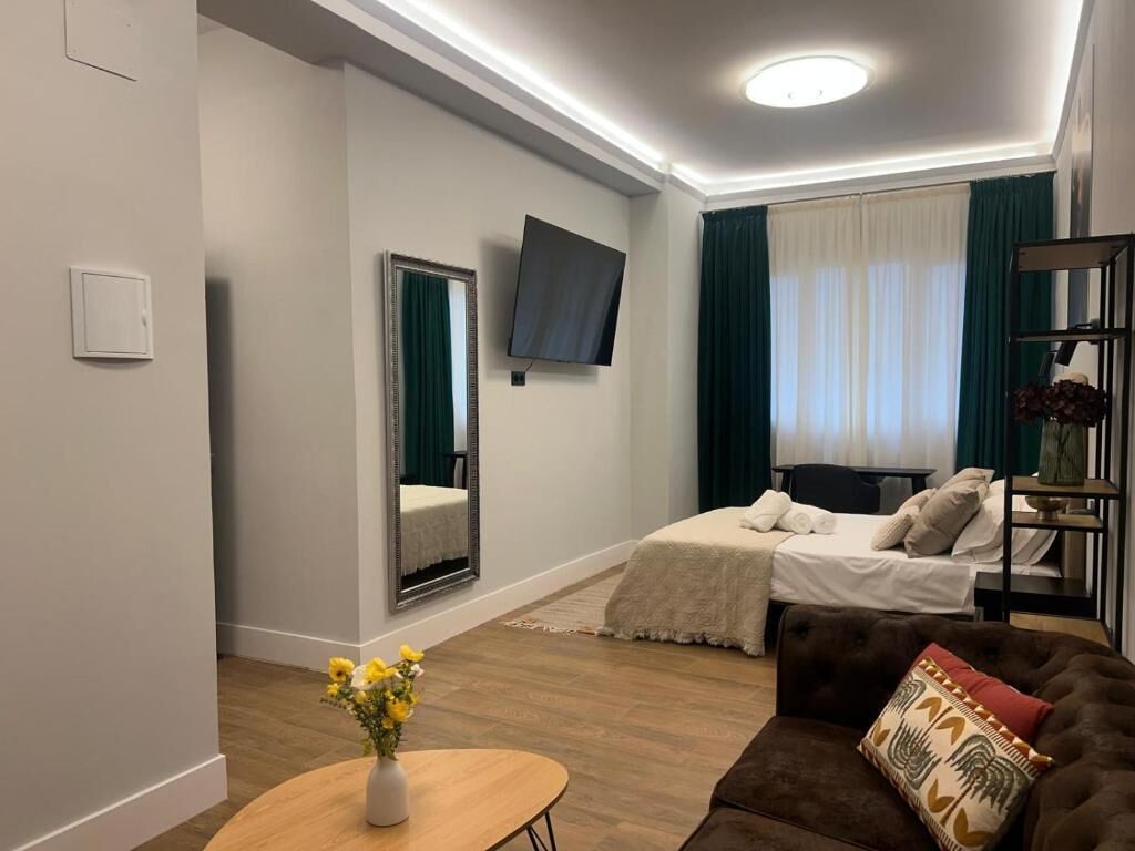 Una habitación de hotel moderna con cama, sofá, televisión y espejo.