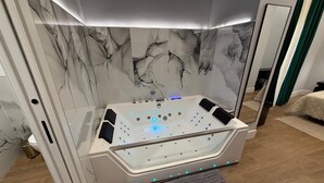 Un baño moderno con un jacuzzi de vidrio, diseño de pared de mármol y un espejo grande.