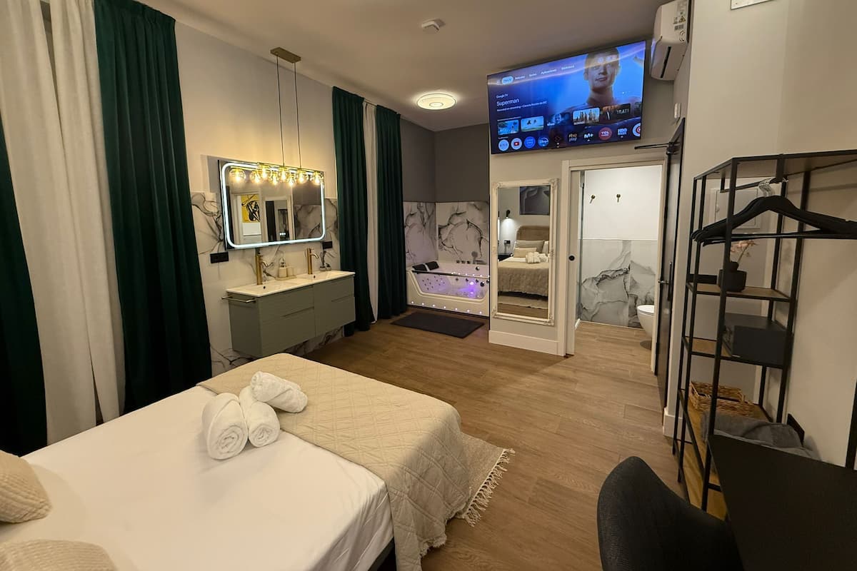 A hotel room with a bed, a vanity with a mirror, a bathtub, and a television displaying a movie.