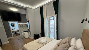 Habitación de hotel con cama, televisor, kitchenette pequeña y balcón.