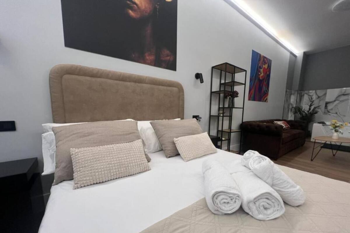A neatly made bed with rolled towels, a headboard, and a bedside table with a lamp.