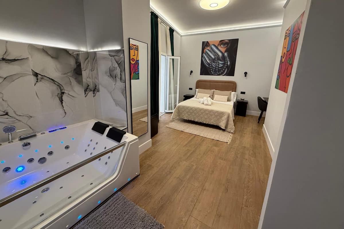 A modern bedroom with a marble wall, a large bed, a built-in jacuzzi, and abstract art on the walls.