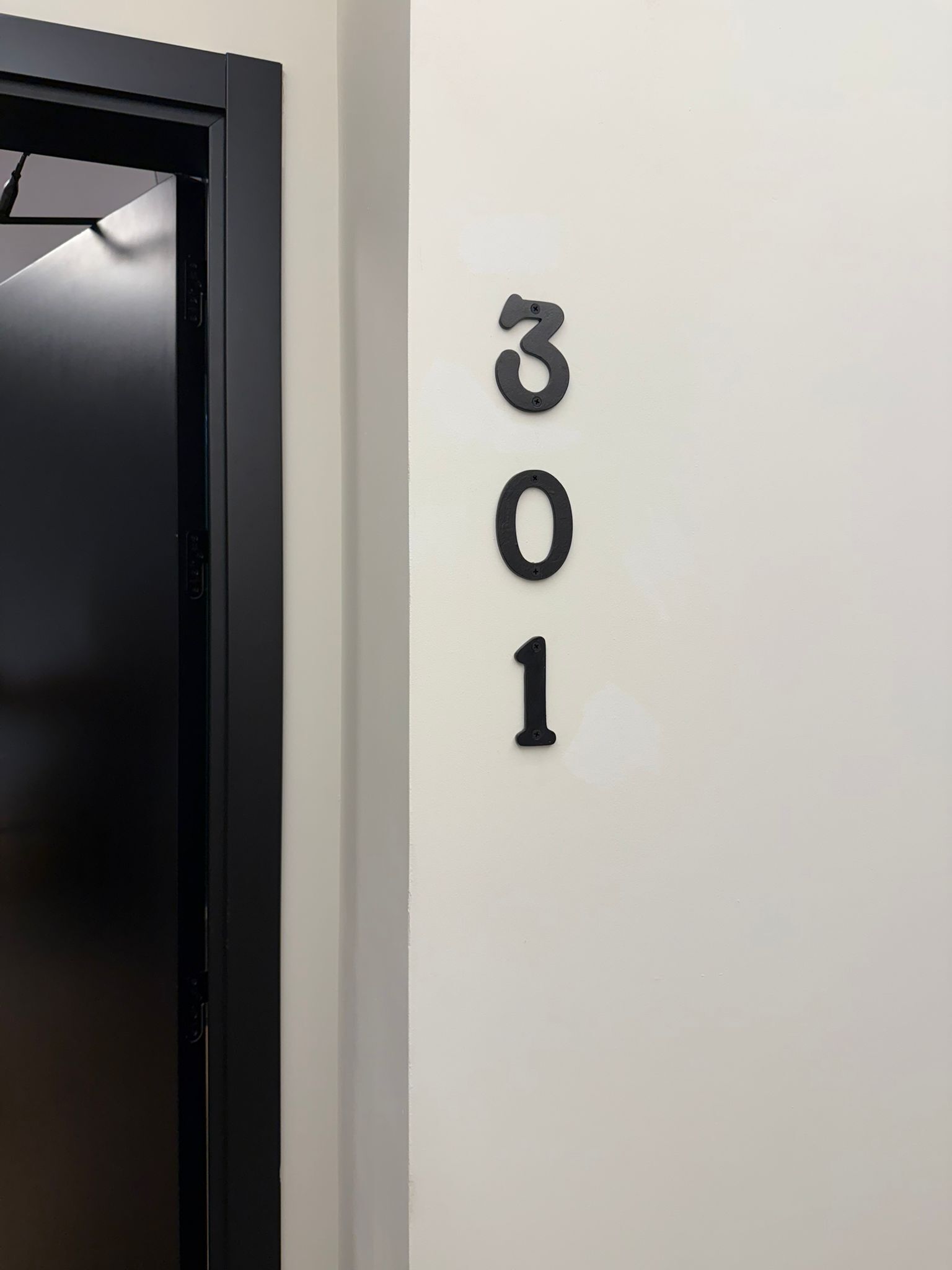 Une porte dotée d’un cadre noir et un mur blanc sur lequel sont fixés les chiffres « 301 ».