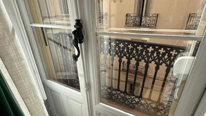 Una habitación con un ventanal grande, paredes blancas con paneles y una barandilla decorativa de metal.