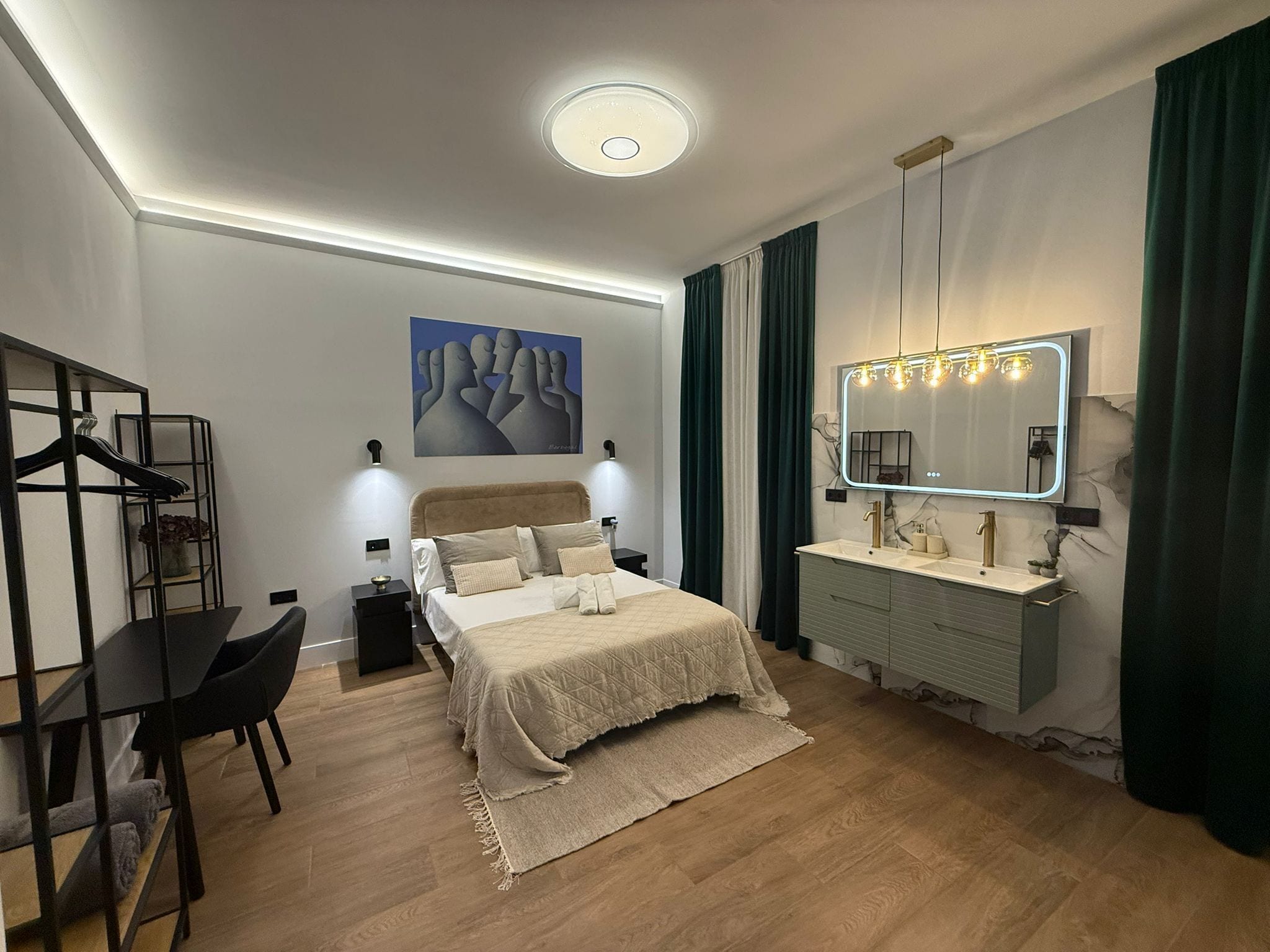 Ein modernes Schlafzimmer mit Bett, Nachttischen, Schreibtisch, Stuhl, Kommode, einem beleuchteten Spiegel und einem Wandbild.