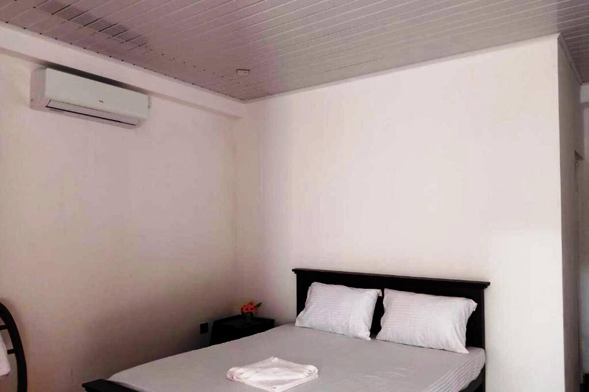 Quarto com cama, mesa de cabeceira e ar condicionado na parede.