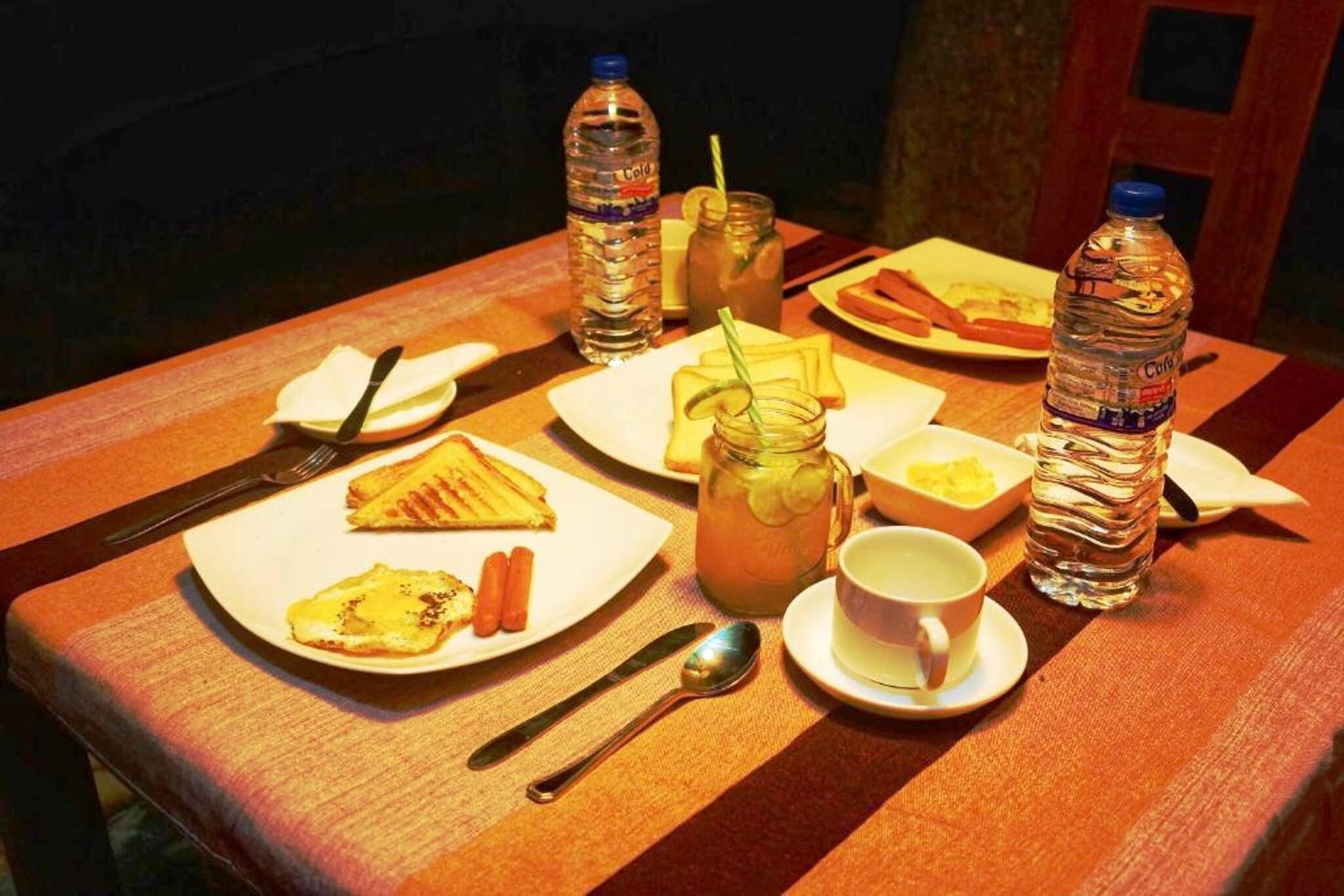 A table set with breakfast items including eggs, sausages, and toast, accompanied by water bottles and a mug.