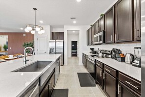 A modern kitchen with a central island, stainless steel appliances, and dark cabinetry. - Resort-Style Living w Private Pool & Amenities (Kissimmee)