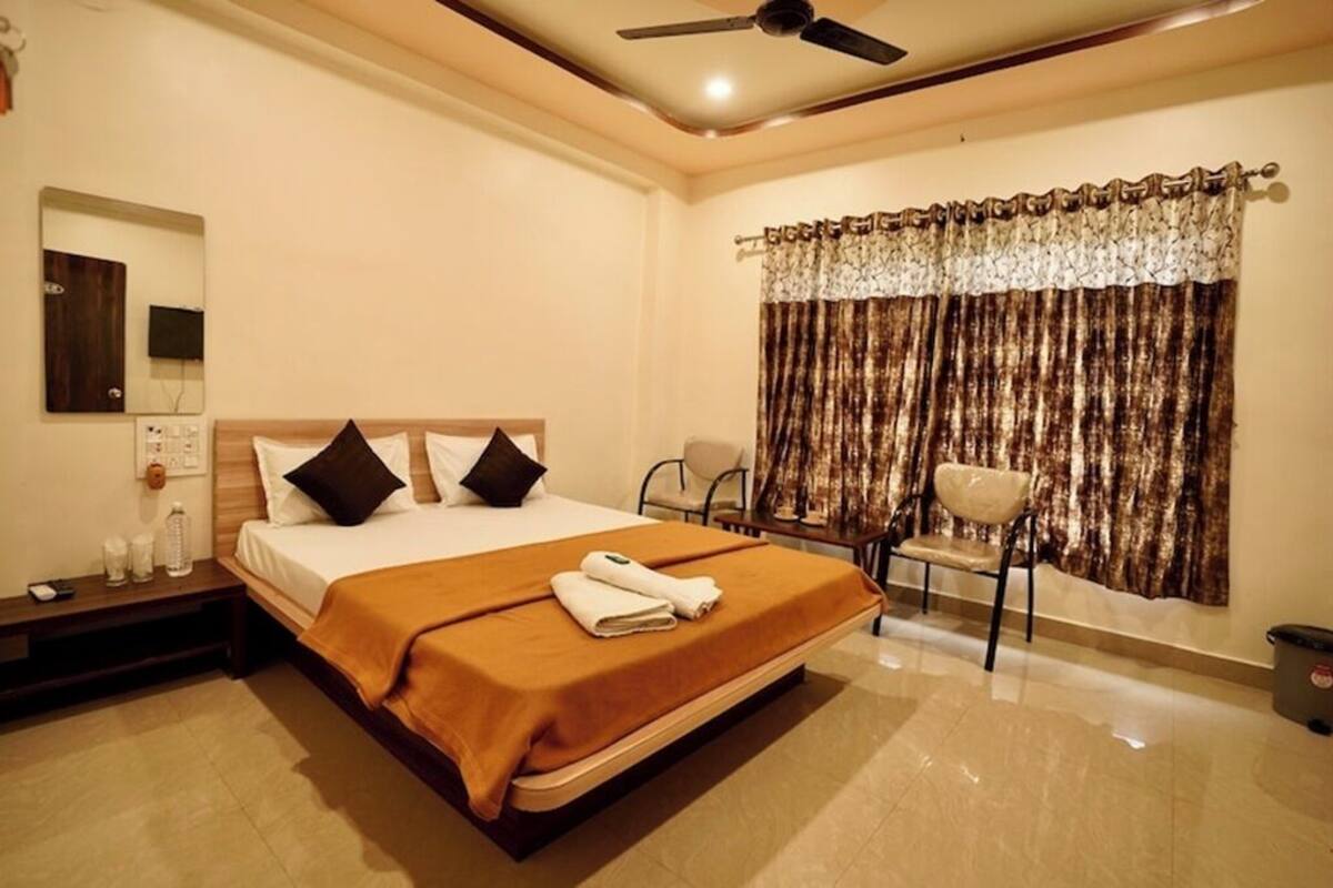 A hotel room with a bed, bedside table, lamp, chair, and curtains.