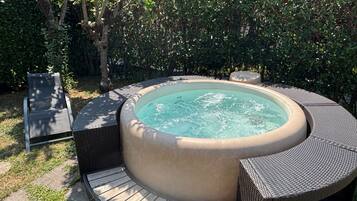 A hot tub with a circular design, surrounded by wicker furniture and a wooden deck.