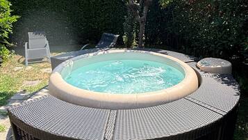 Ein Whirlpool, umgeben von einer Rattan-Terrasse, mit einem Baum und einer Hecke im Hintergrund.