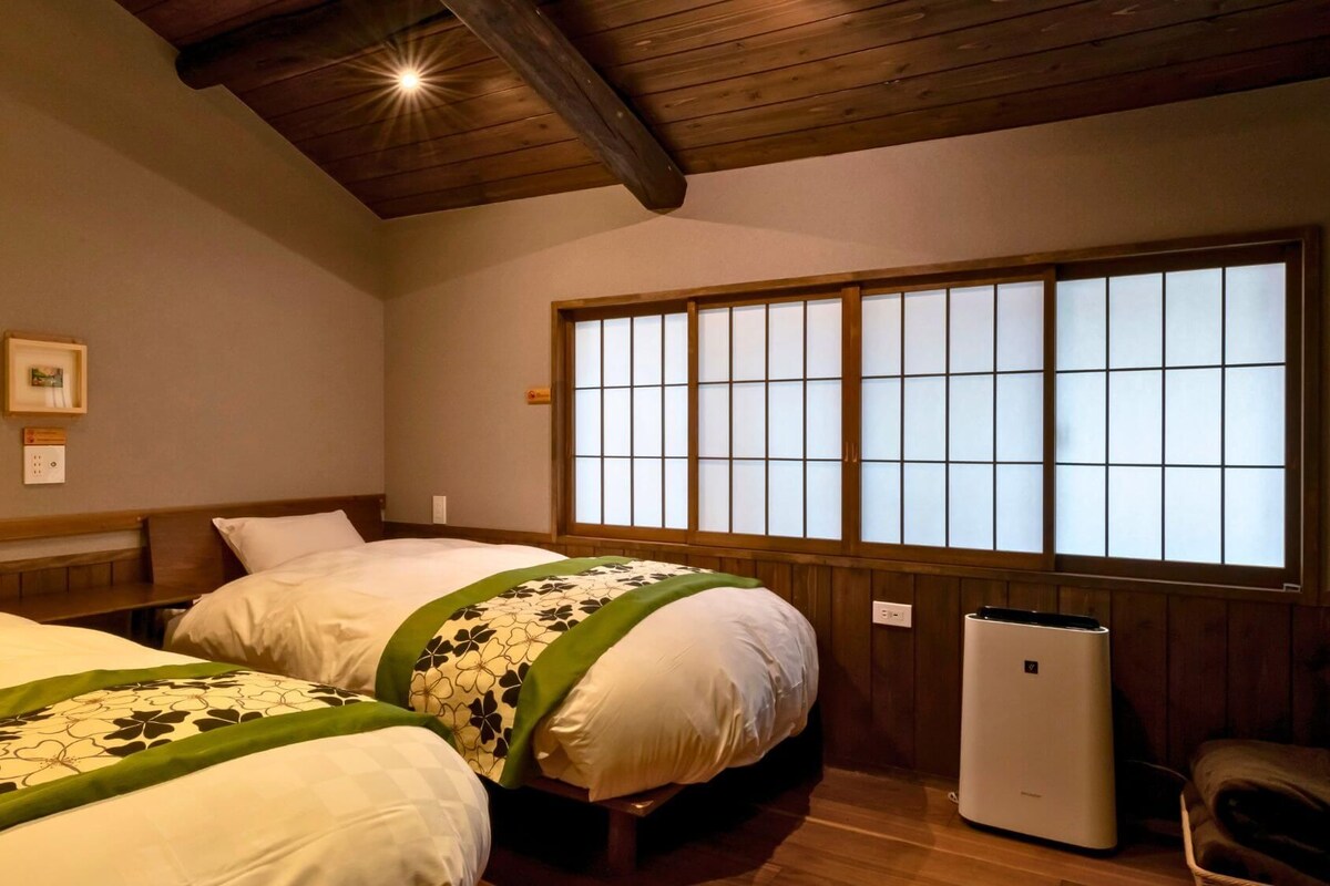 A hotel room with two beds, a large window with a view, and a heater on the floor.