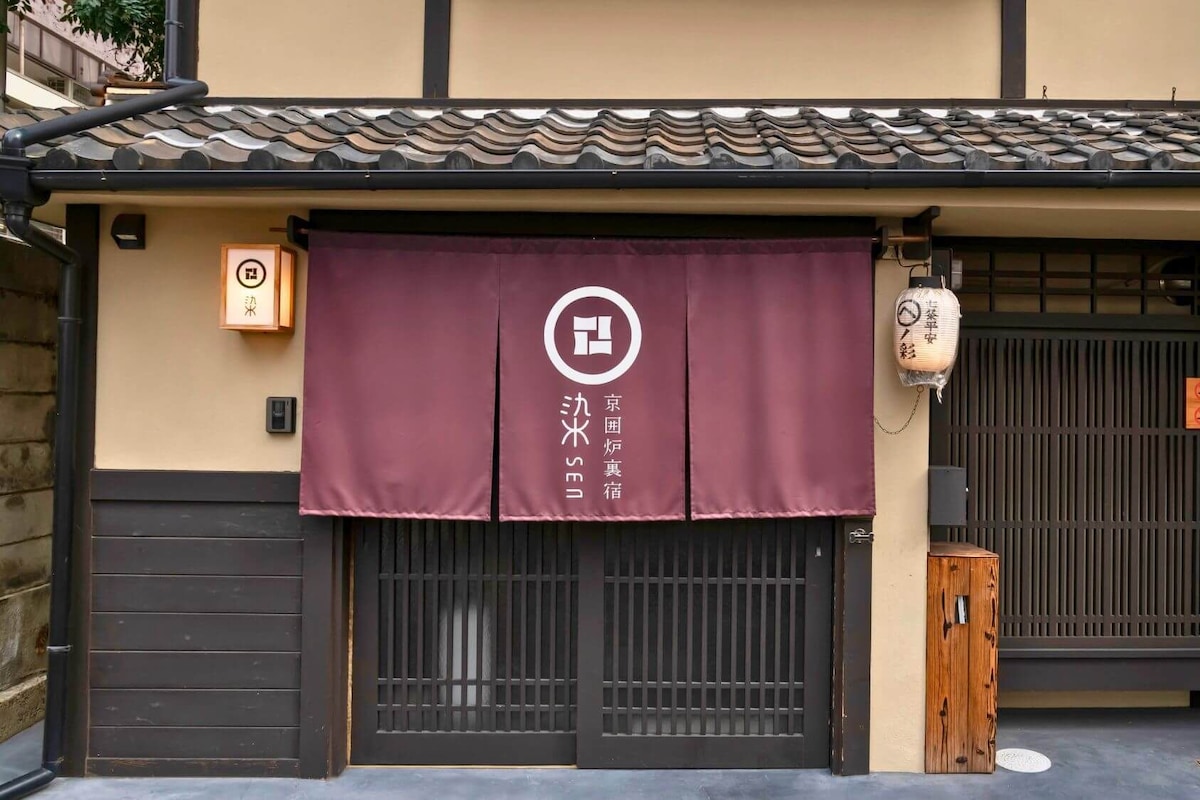 A traditional Japanese building with a tiled roof, a wooden door, and a purple awning with a logo.
