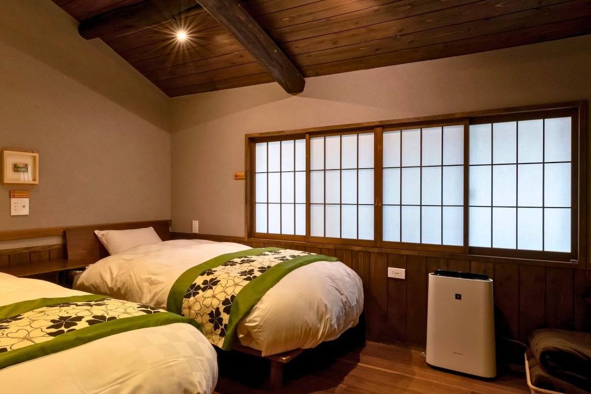 A hotel room with two beds, a large window with a view, and a heater on the floor.