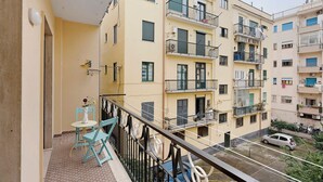 Un edificio residencial de varios pisos con balcones, una pequeña zona de estar al aire libre y un coche estacionado.