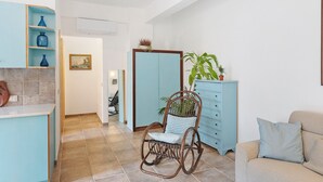 Una habitación con una mecedora, un armario azul claro, un sofá beige y suelo de baldosas.