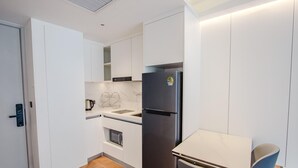 Eine kleine Küche mit weißen Schränken, einem eingebauten Backofen, einem Edelstahlkühlschrank und einem kleinen Esstisch mit Stühlen.
