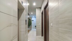 A hallway with marble walls and a tiled floor, leading to an elevator and a green door. - Hotel Siya Ram by AKC Hotels (Haridwar)
