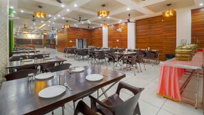 A spacious dining area with multiple tables and chairs, ceiling fans, and modern lighting fixtures. - Hotel Siya Ram by AKC Hotels (Haridwar)