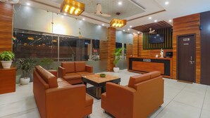 A modern hotel lobby with leather sofas, a reception desk, and a television. - Hotel Siya Ram by AKC Hotels (Haridwar)