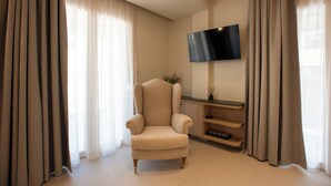 Un soggiorno con una poltrona beige, una TV a schermo piatto montata a parete e un tavolino consolle in legno.