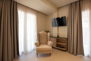 Ein Wohnzimmer mit einem beigefarbenen Sessel, einem flachbildfernseher an der Wand und einem Holztische.
