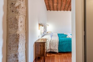 Ein Schlafzimmer mit einem Bett, einem Nachttisch, einer Wandleuchte und einer Holzbalkendecke.