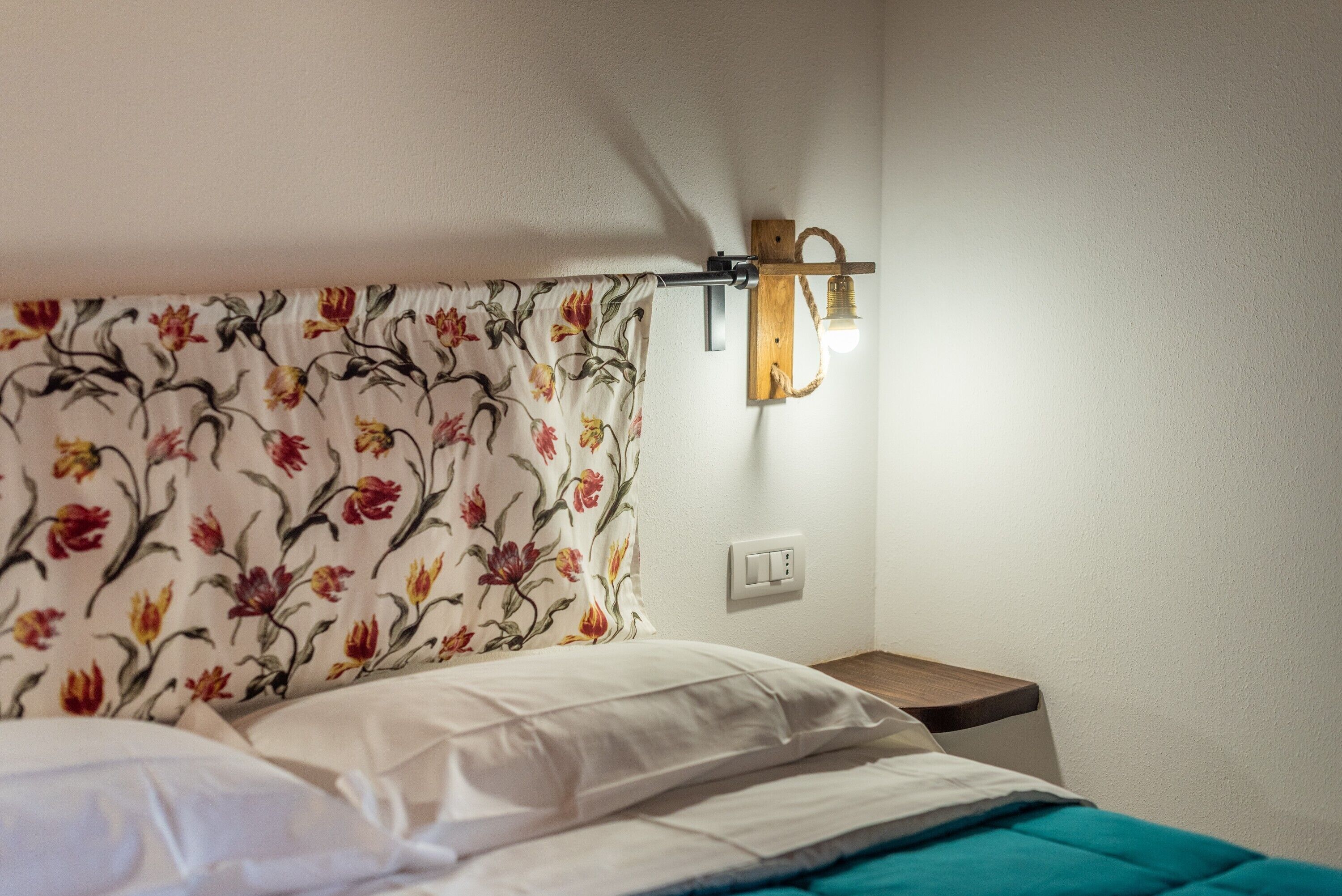 Ein Schlafzimmer mit einem blumengemusterten Kopfteil, einem Nachttisch mit Lampe und einer Steckdose an der Wand.