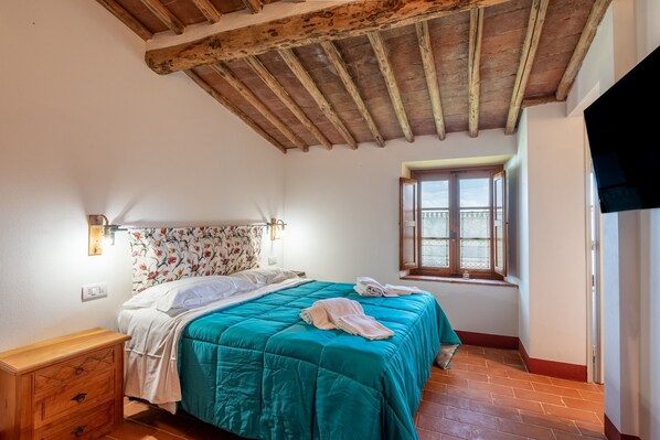 Une chambre avec un plafond en bois, un lit avec une literie de couleur turquoise, une table de chevet en bois, une fenêtre avec vue et un luminaire fixé au mur.