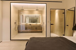 A modern bedroom with a glass-enclosed shower, a large mirror, and a bed with a dark headboard. - Villa Socrate with pool and gym - My Rental Homes (Mykonos)
