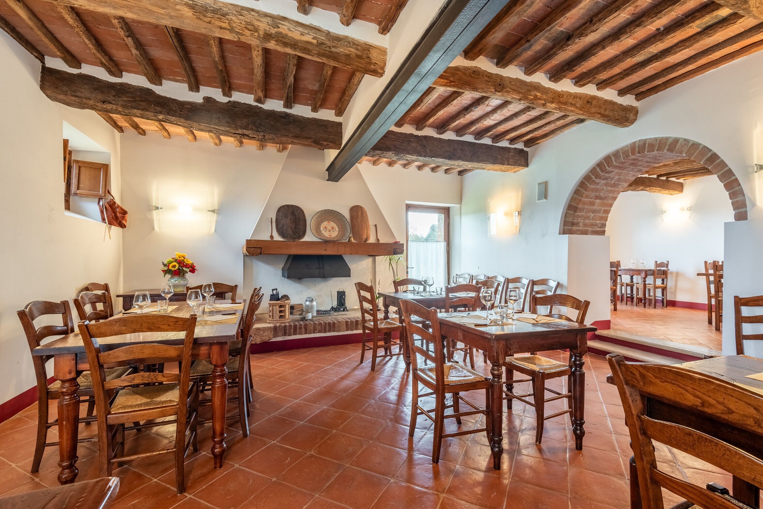 Un espace repas avec des tables et des chaises en bois, une cheminée en briques et des poutres apparentes au plafond.
