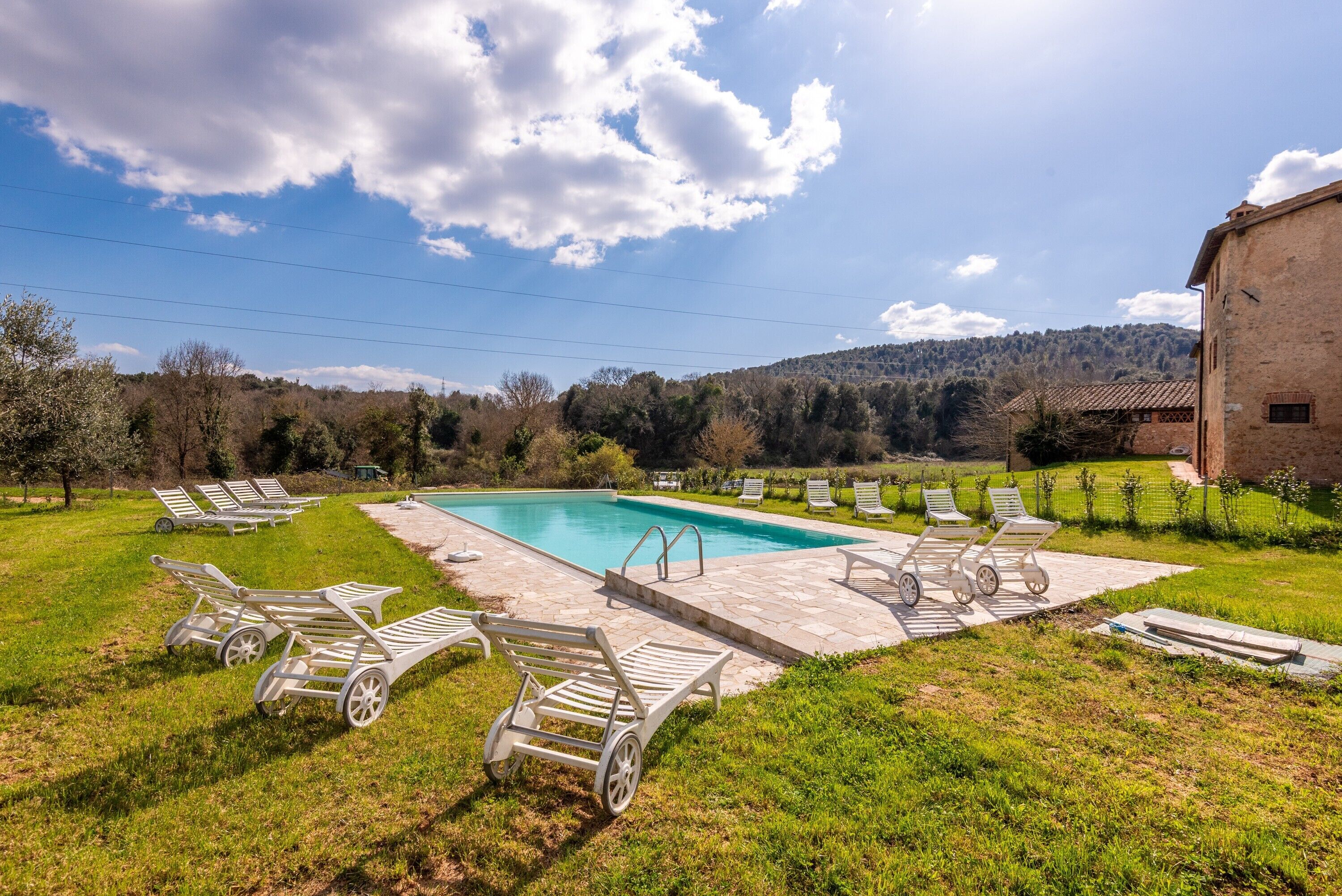 Une piscine avec des chaises longues, un bâtiment en briques et un paysage vallonné en arrière-plan.
