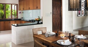 Une cuisine moderne dotée d’un îlot central, de meubles en bois et d’un coin repas avec une table en bois mise pour deux personnes.