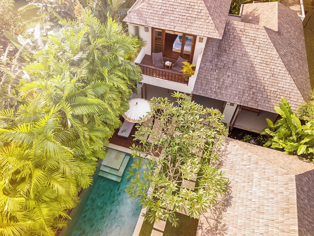 A two-story house with a swimming pool, surrounded by lush greenery.