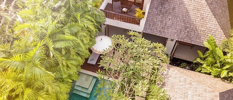 A two-story house with a swimming pool, surrounded by lush greenery.
