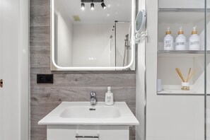 A bathroom with a white sink, a mirror, and a shower area. There are toiletries on a shelf. - B&B Apartments. Modern and Luxurious Apartment Less Than 100 Meters from the Beach (La Cala de Mijas)