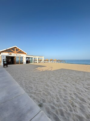 A beachside building with a sign reading 'Los Moreno,' a sandy beach, and umbrellas.