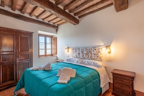 A bedroom with a wooden ceiling, a bed with a teal bedspread, a nightstand, and a wardrobe. - Room 'Cetinale' - Agriturismo la Taverna di Celsa with Shared Pool (Sovicille)