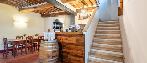 Un interior rústico con vigas de madera a la vista, una barra de madera, una escalera y un comedor con sillas y mesa de madera.
