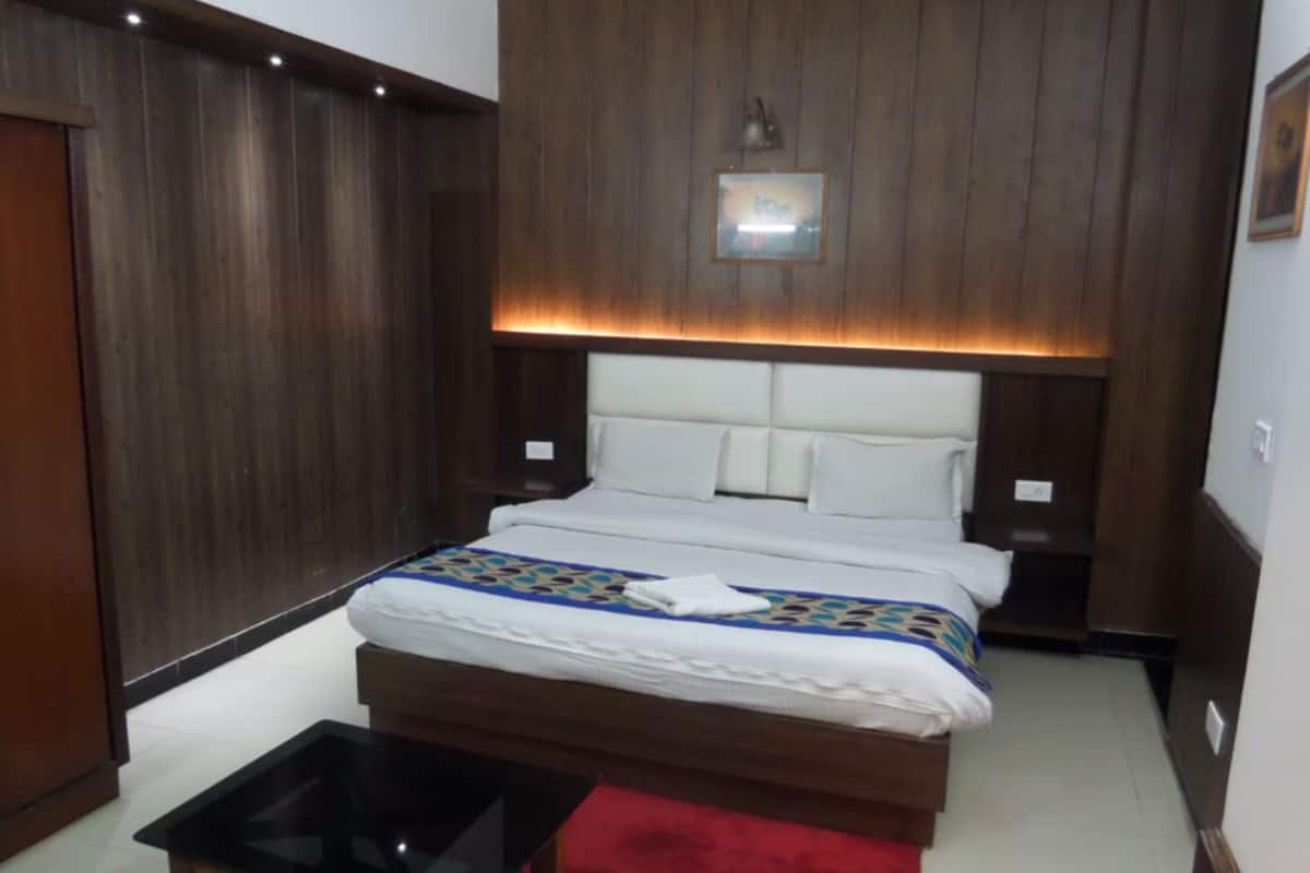 Une chambre à coucher avec une tête de lit en bois, un lit recouvert de draps blancs, une petite table et un tapis rouge.