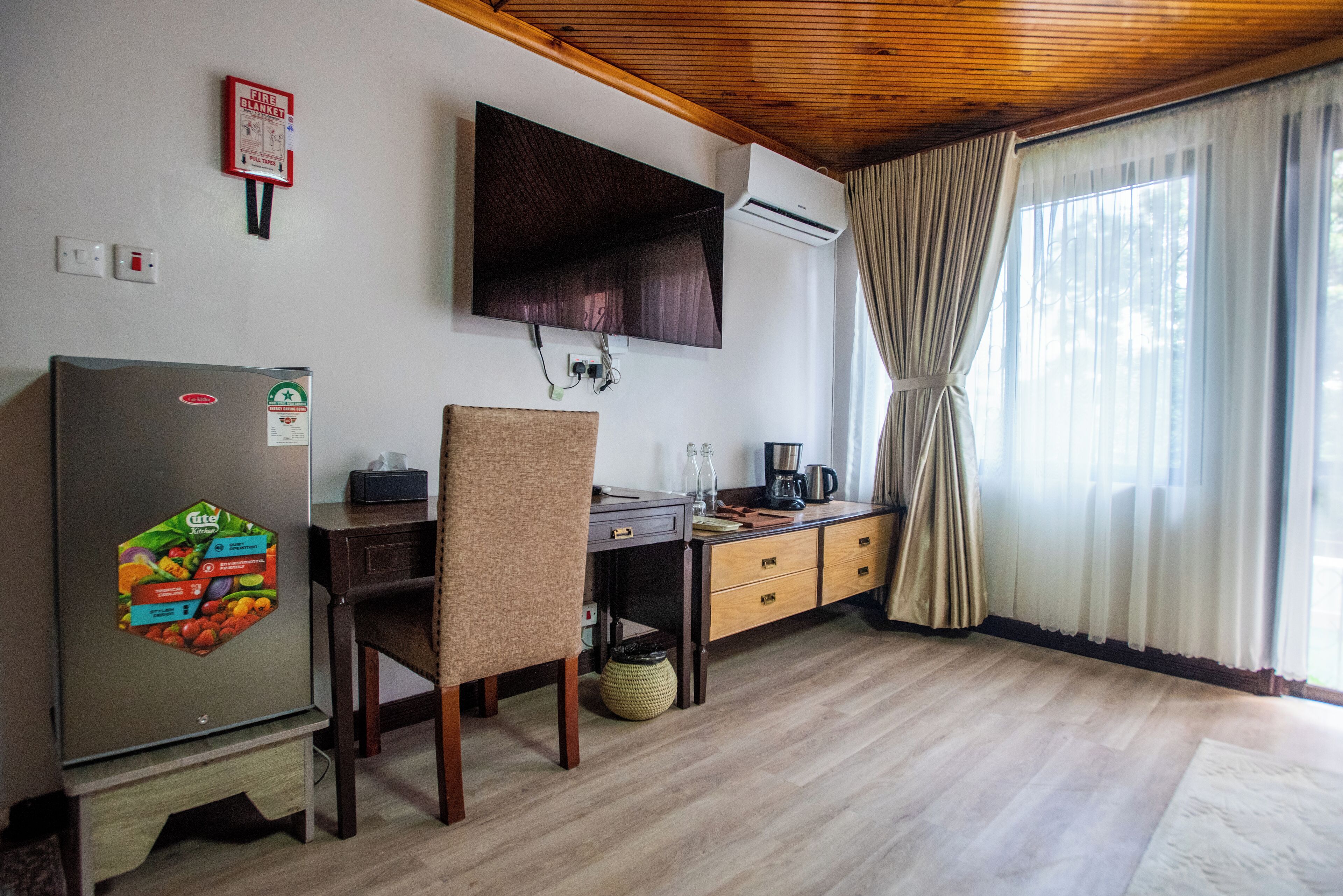 Una cocina con refrigerador, una mesa de comedor de madera, una silla, cafetera y una ventana con cortinas.
