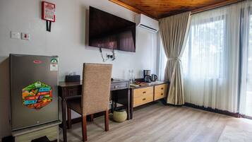 Una cocina con refrigerador, una mesa de comedor de madera, una silla, cafetera y una ventana con cortinas.