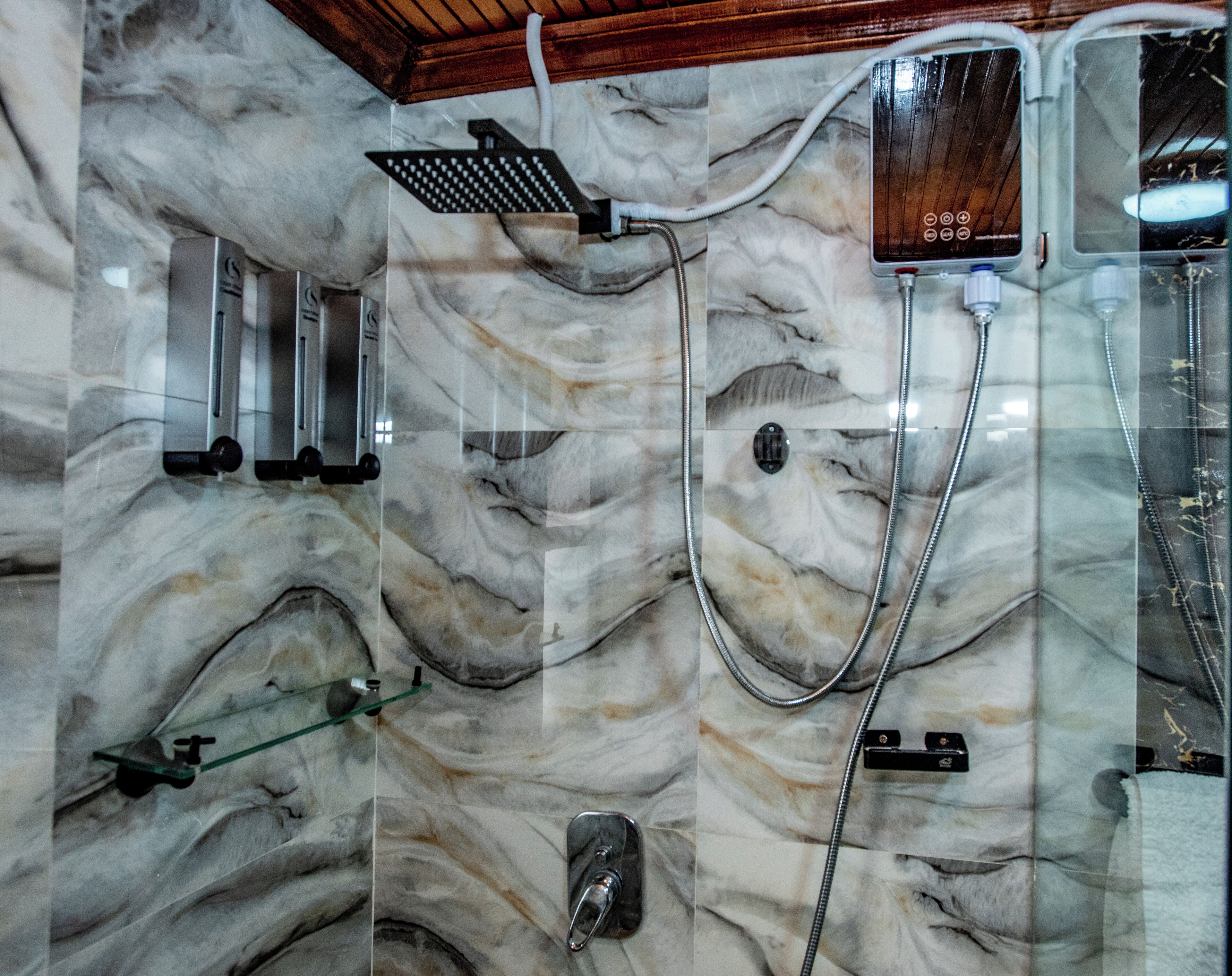 Un baño con pared de mármol, ducha con panel de control y lavamanos con cerramiento de vidrio.