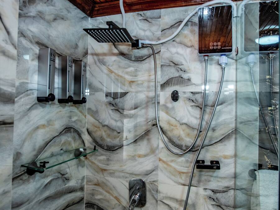 Un baño con pared de mármol, ducha con panel de control y lavamanos con cerramiento de vidrio.