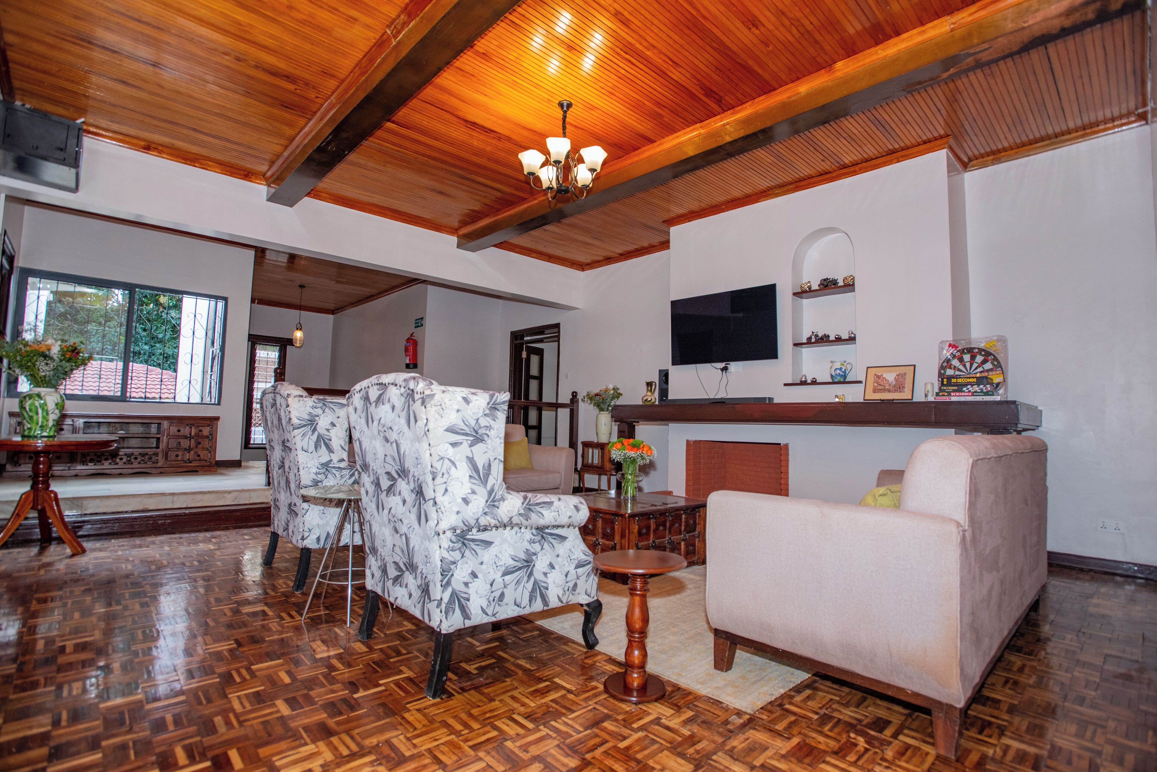 Een ruime woonkamer met houten plafond, open haard, televisie en een eethoek met tafel en stoelen.