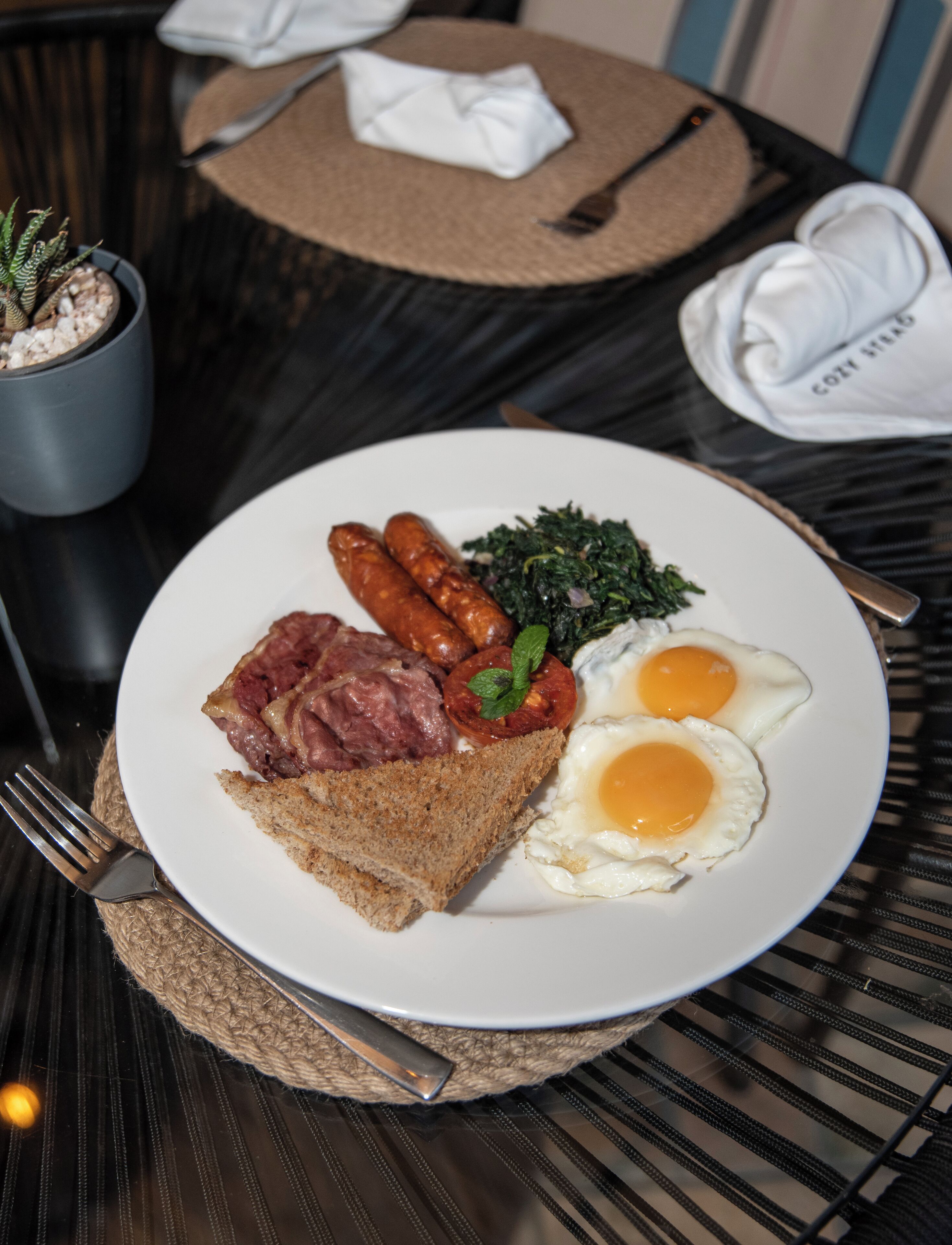 A plate of breakfast food including eggs, sausages, and toast, served on a white plate with a fork on the side.