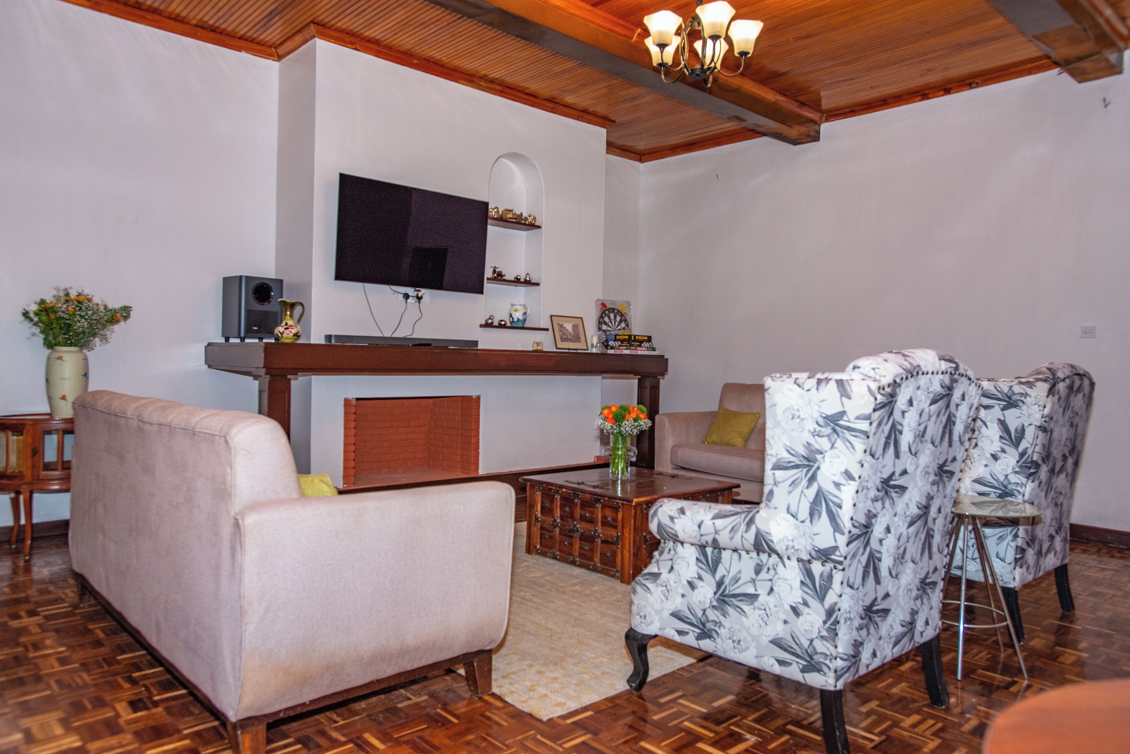 Una sala de estar con un sofá, un sillón y una mesa de centro. Hay un televisor de pantalla plana montado en la pared, un aparador de madera y una mesita con adornos.