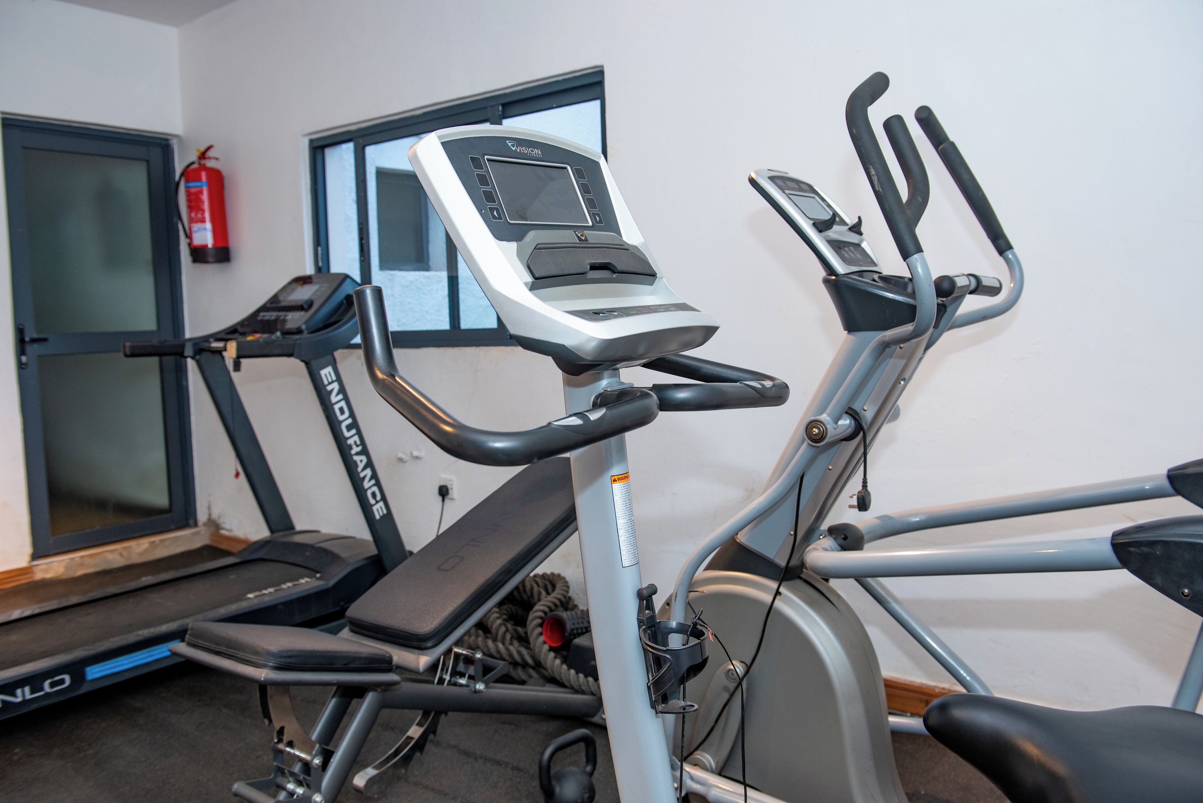 Un gimnasio con equipo de ejercicio, incluyendo una cinta de correr, una máquina elíptica y una bicicleta estática.